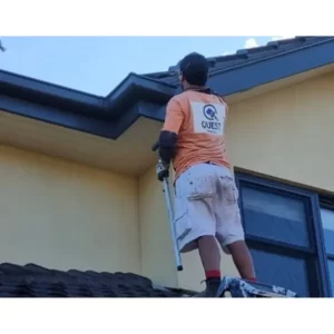 A man on a roof with a ladder and a tool, representing skilled house painters in Dandenong at work on a project.